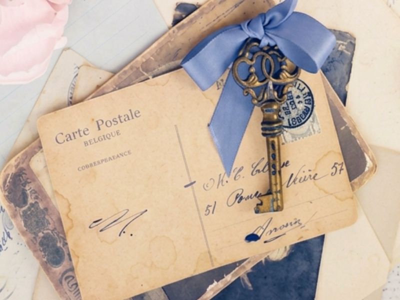 Vintage postcards and artifacts from an immersive epistolary subscription, featuring an ornate old key tied with a blue bow over handwritten correspondence.