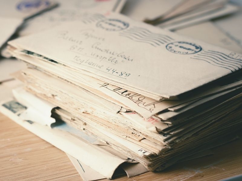 Close-up shot of a thick stack of old, vintage handwritten letters and envelopes with postal stamps, resting on a wooden surface.